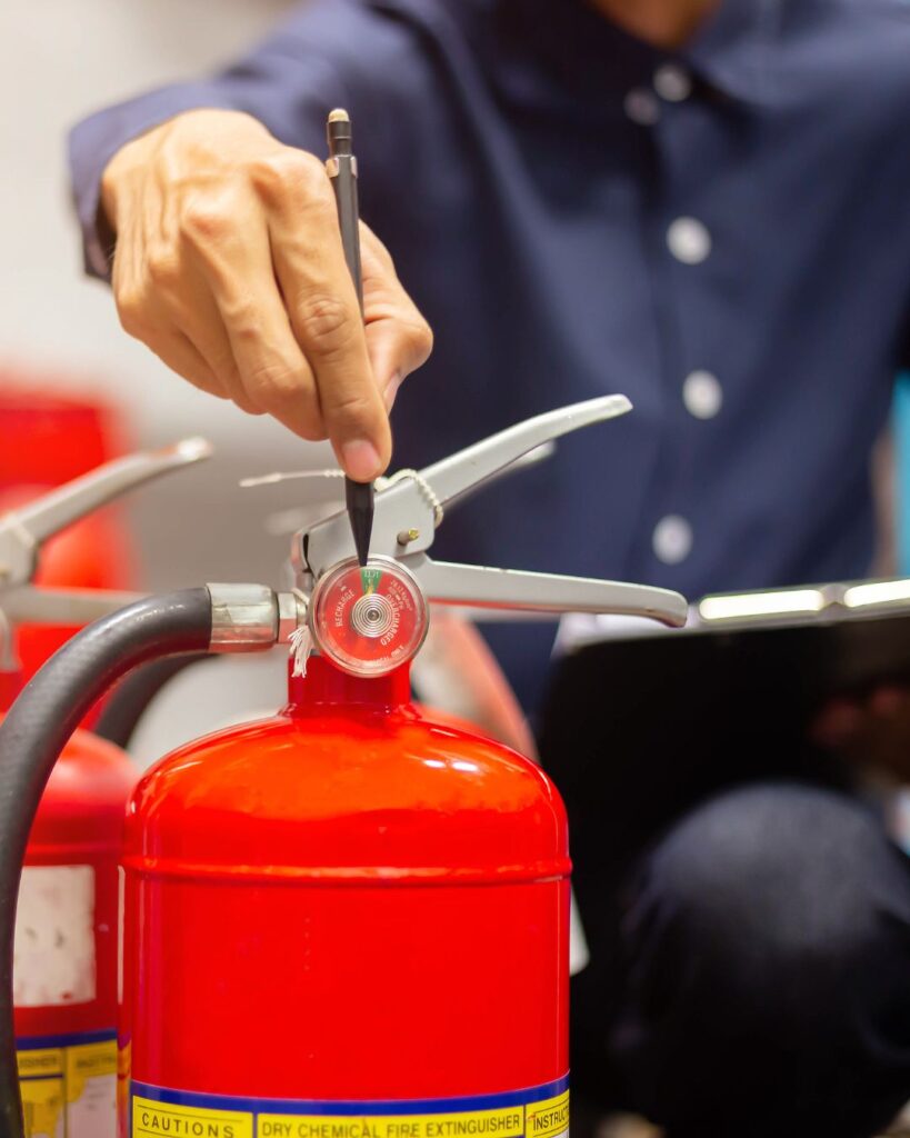 Osoba sprawdzająca gaśnicę podczas przeglądu sprzętu przeciwpożarowego