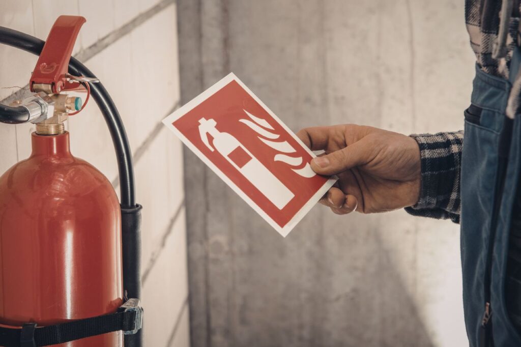 Osoba umieszczająca znak gaśnicy na ścianie przy sprzęcie PPOŻ